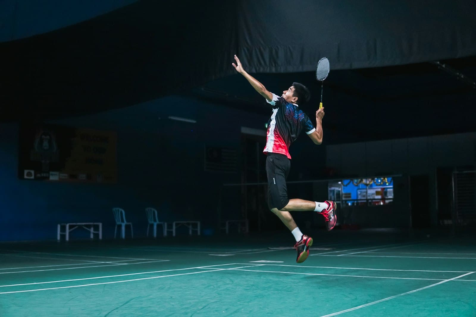 Badminton player mid-jump smash on an indoor court